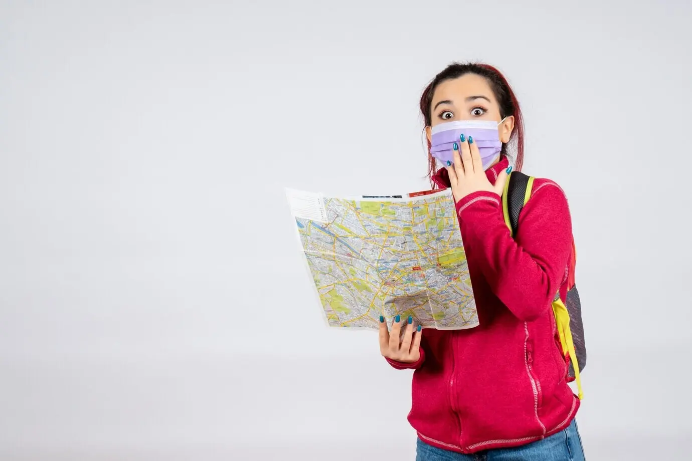 Vorderansicht einer Touristin mit Karte und Maske vor weißer Wand, Virus